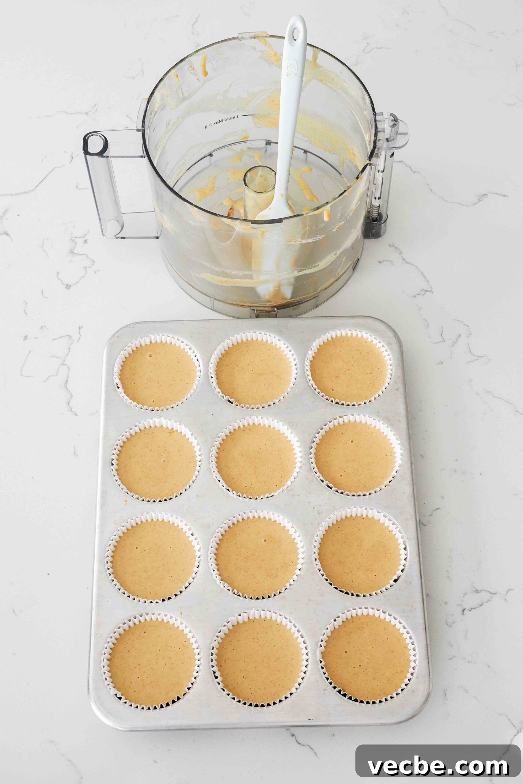 Mini Pecan Pie Cheesecake Bites Recipe 10 An empty food processor bowl next to a muffin pan filled with unbaked mini cheesecakes.