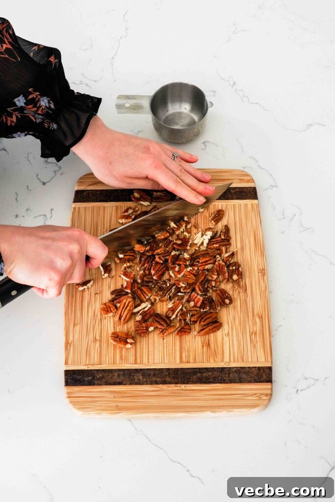 Mini Pecan Pie Cheesecake Bites Recipe 13 A woman roughly chops pecans on a wooden cutting board.