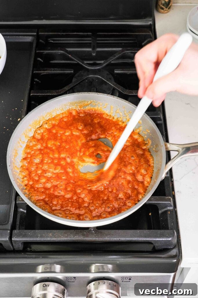 Mini Pecan Pie Cheesecake Bites Recipe 15 A spatula stirs heavy cream into a sauté pan with dark caramel sauce. over the stove.