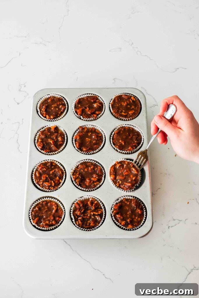 Mini Pecan Pie Cheesecake Bites Recipe 18 A hand slides a fork under a mini pecan cheesecake to pop it out of a muffin pan.