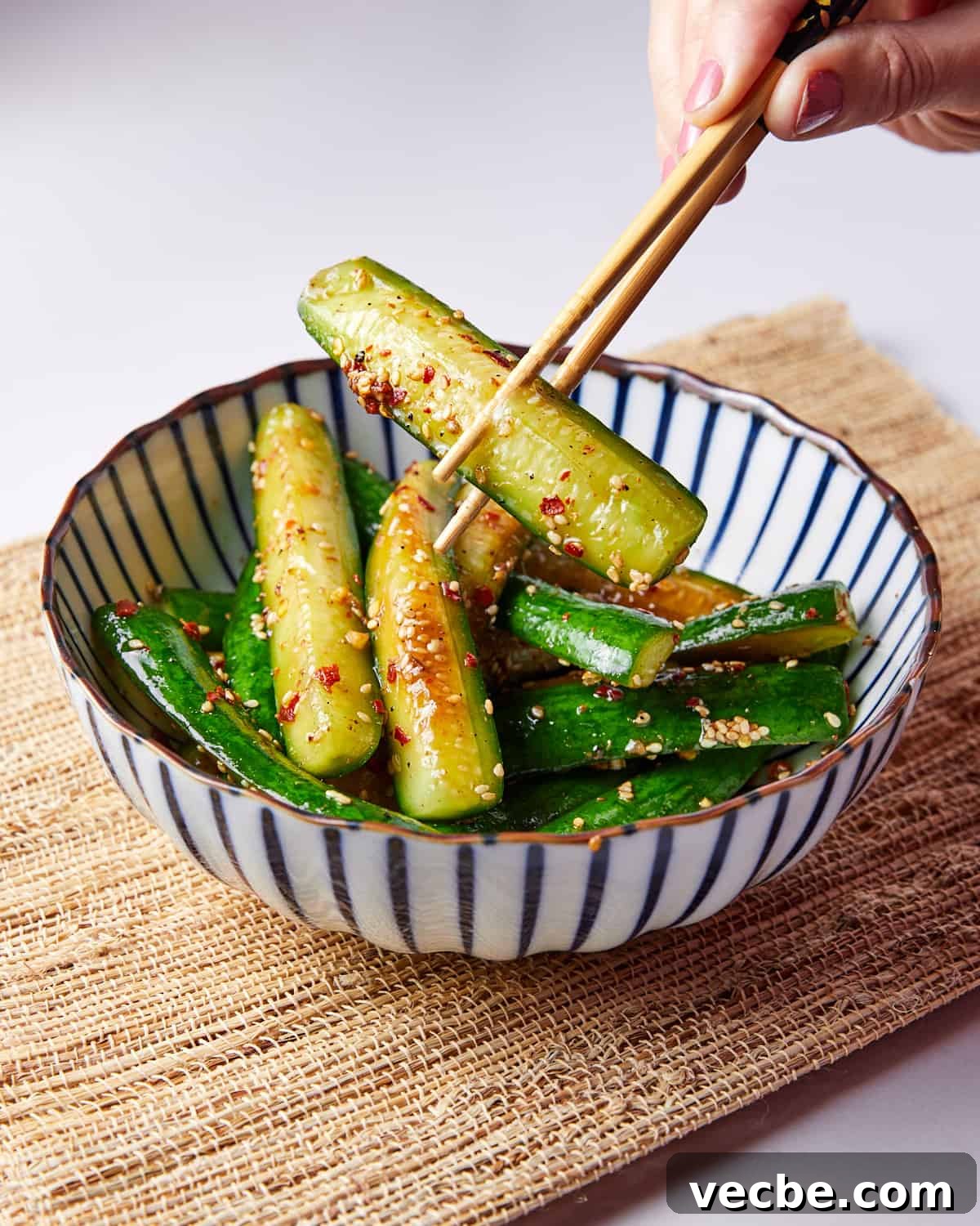 Quick Chinese Pickled Cucumbers Recipe 11 Photo of someone using chopsticks to take a piece of Chinese quick pickled cucumber out of a blue and white striped bowl.