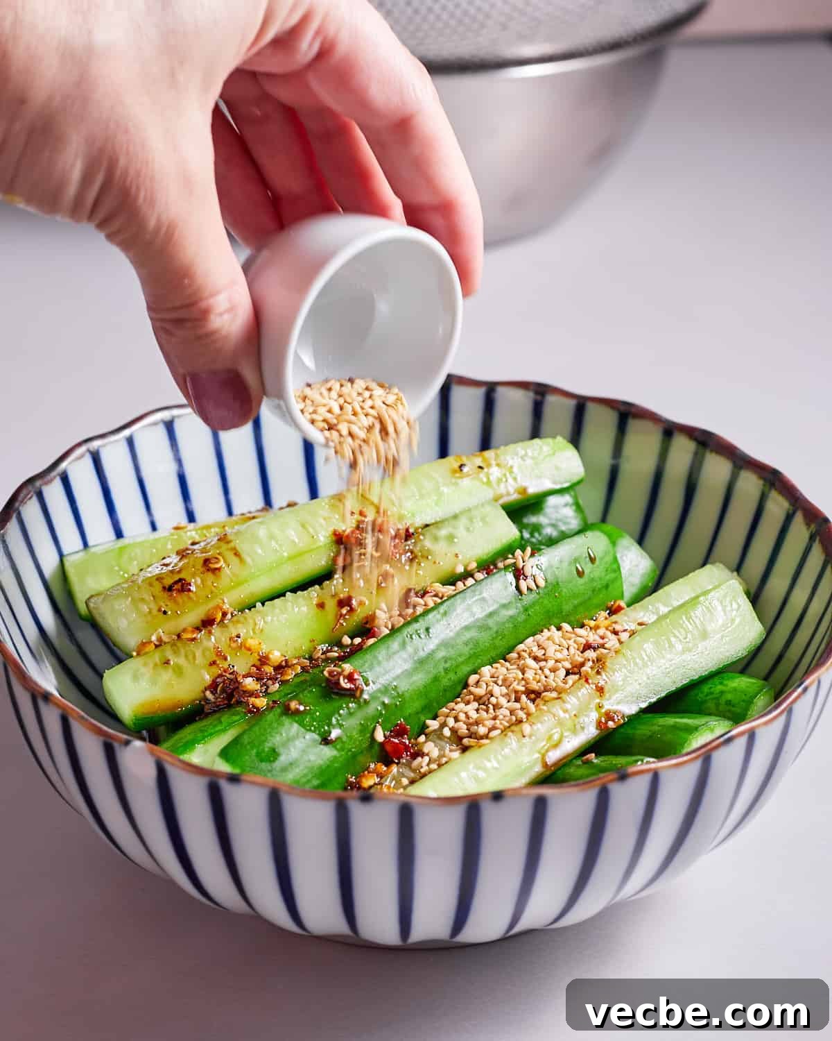 Quick Chinese Pickled Cucumbers Recipe 12 Photo of someone pouring sesame seeds onto a bowl of Chinese pickled cucumbers.