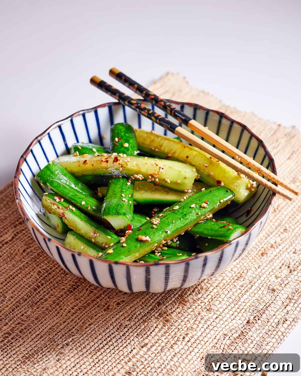 Quick Chinese Pickled Cucumbers Recipe 10 Photo of pickled cucumbers in a white and blue stripy bowl with chopsticks.