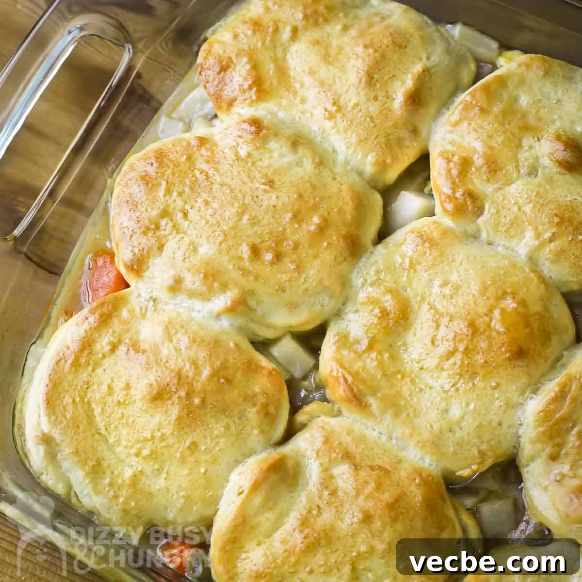 Creamy Slow Cooker Chicken and Biscuits 11 Overhead close up shot of chicken and biscuits in a clear baking dish on a wooden surface.