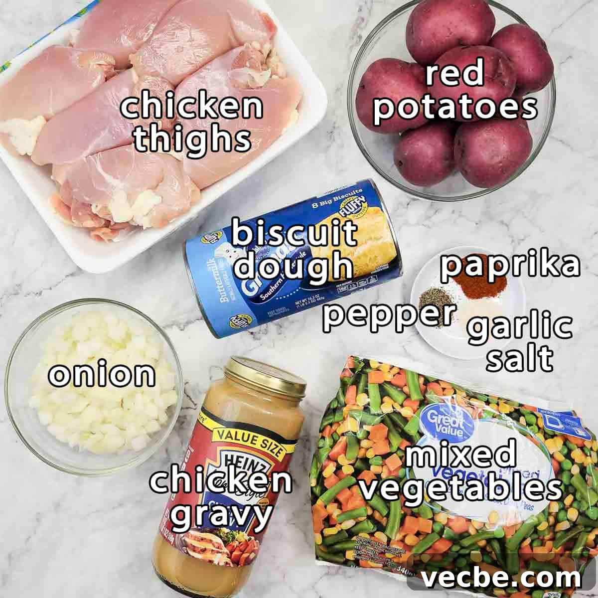 Creamy Slow Cooker Chicken and Biscuits 3 Overhead shot of ingredients - chicken thighs, red potatoes, biscuit dough, onion, chicken gravy, mixed vegetables, paprika, pepper, and garlic salt.