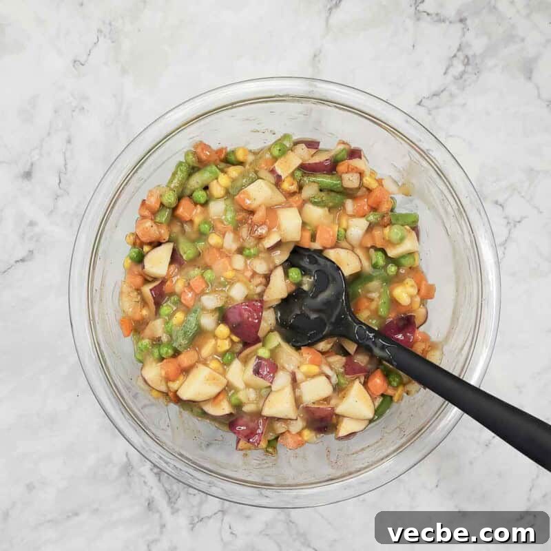 Creamy Slow Cooker Chicken and Biscuits 5 Overhead view of process shot 2 - combine the potatoes, gravy, mixed veggies, onion, garlic, salt, pepper, and paprika in a bowl.