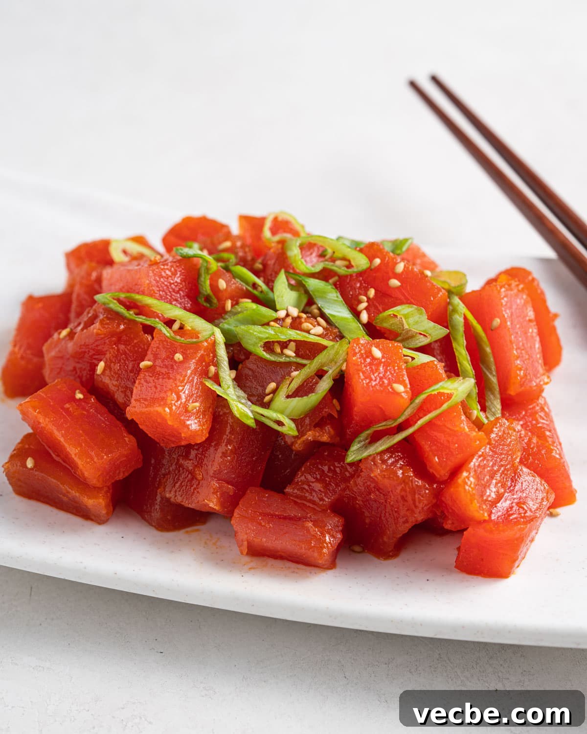 Spicy Tuna Recipe with Sriracha Mayo 2 Side angle of spicy tuna topped with green onions and sesame seeds on a plate with chopsticks on the side.