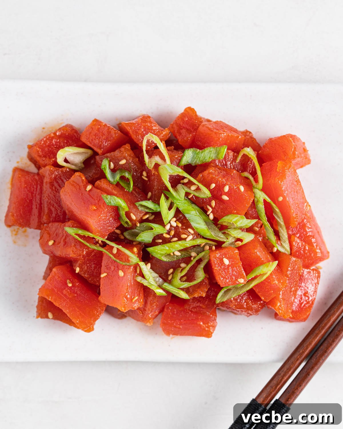 Spicy Tuna Recipe with Sriracha Mayo 6 spicy tuna topped with green onions and sesame seeds on a plate with chopsticks on the side.