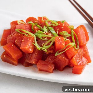 Spicy Tuna Recipe with Sriracha Mayo 7 spicy tuna topped with green onions and sesame seeds on a plate with chopsticks on the side.