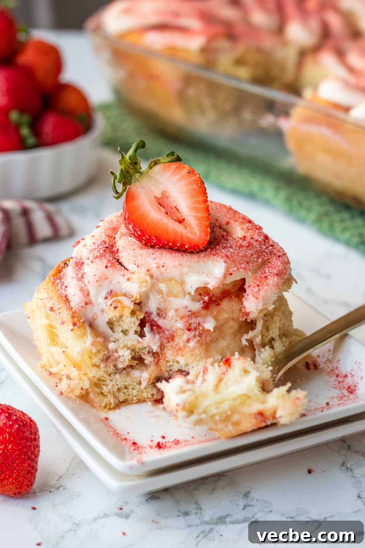 Strawberry Cheesecake Cinnamon Rolls Recipe 11 Baked strawberry roll on white plate with bite removed.