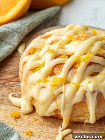 Baked frosted orange roll on wooden cutting board.