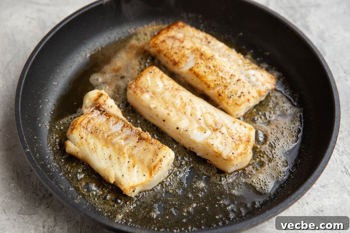 Pan-Fried Mediterranean Cod with Lemon, Olives and Tomatoes 5 Three cod fillets cooking in a nonstick skillet in butter and oil with a golden brown sear on the outside.