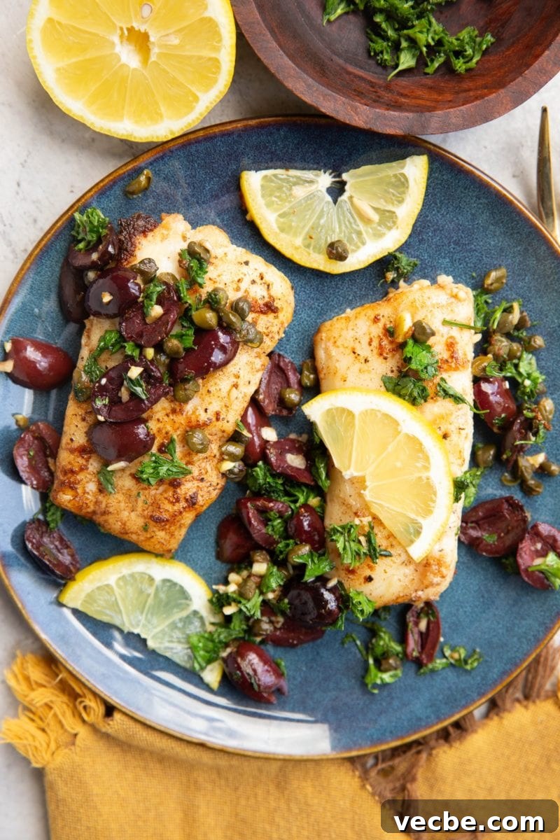 Pan-Fried Mediterranean Cod with Lemon, Olives and Tomatoes 8 Two cod fillets on a blue plate sprinkled with olives, capers, parsley and lemon slices. Ready to serve.