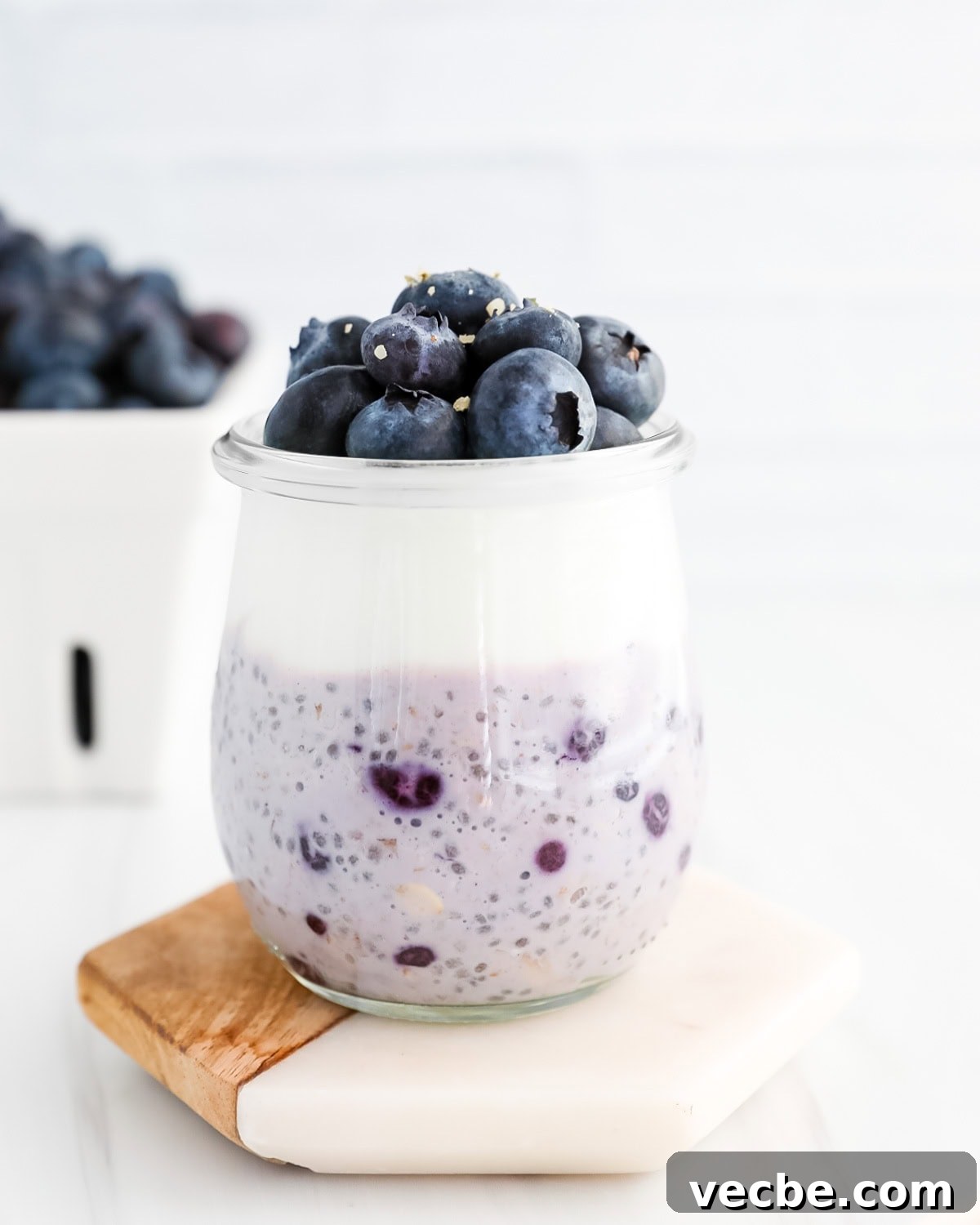 Creamy Blueberry Overnight Oats Recipe 2 A clear glass jar filled with bright blue/purple overnight oats with a layer of yogurt and fresh blueberries on top.