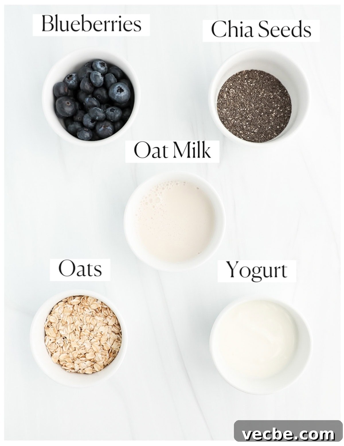 Creamy Blueberry Overnight Oats Recipe 3 5 white bowls filled with labeled ingredients including: blueberries, chia seeds, oat milk, oats, and yogurt.