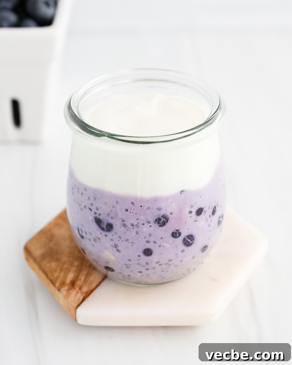 Creamy Blueberry Overnight Oats Recipe 4 A clear jar filled with a layer of blueberry oats at the bottom and a layer of vanilla yogurt on top.