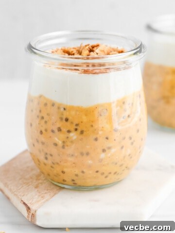 Pumpkin overnight oats in a glass jar topped with a layer of vanilla yogurt and granola.