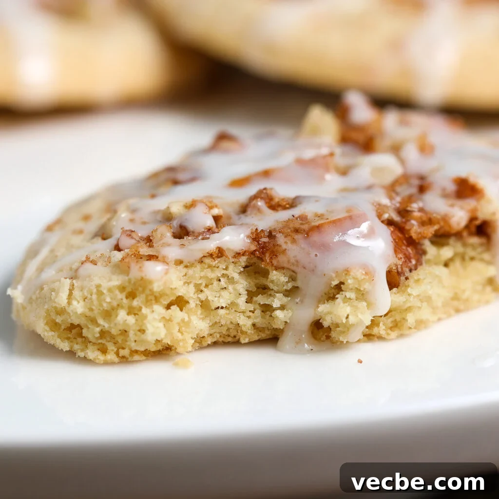 Coffee Cake Cookies with Cinnamon Streusel 3 A close-up of a soft cookie with a cinnamon swirl and white icing drizzled on top, resting on a white plate. Reminiscent of coffee cake donuts, the cookie appears thick, chewy, and freshly baked.