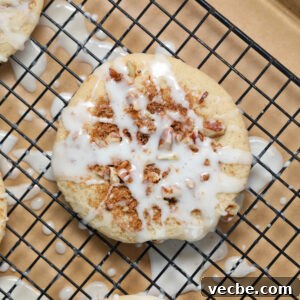 Coffee Cake Cookies with Cinnamon Streusel 4 A close-up of a round, baked coffee cake donut topped with crumbled cinnamon filling and drizzled with white icing, resting on a black wire cooling rack lined with brown parchment paper.