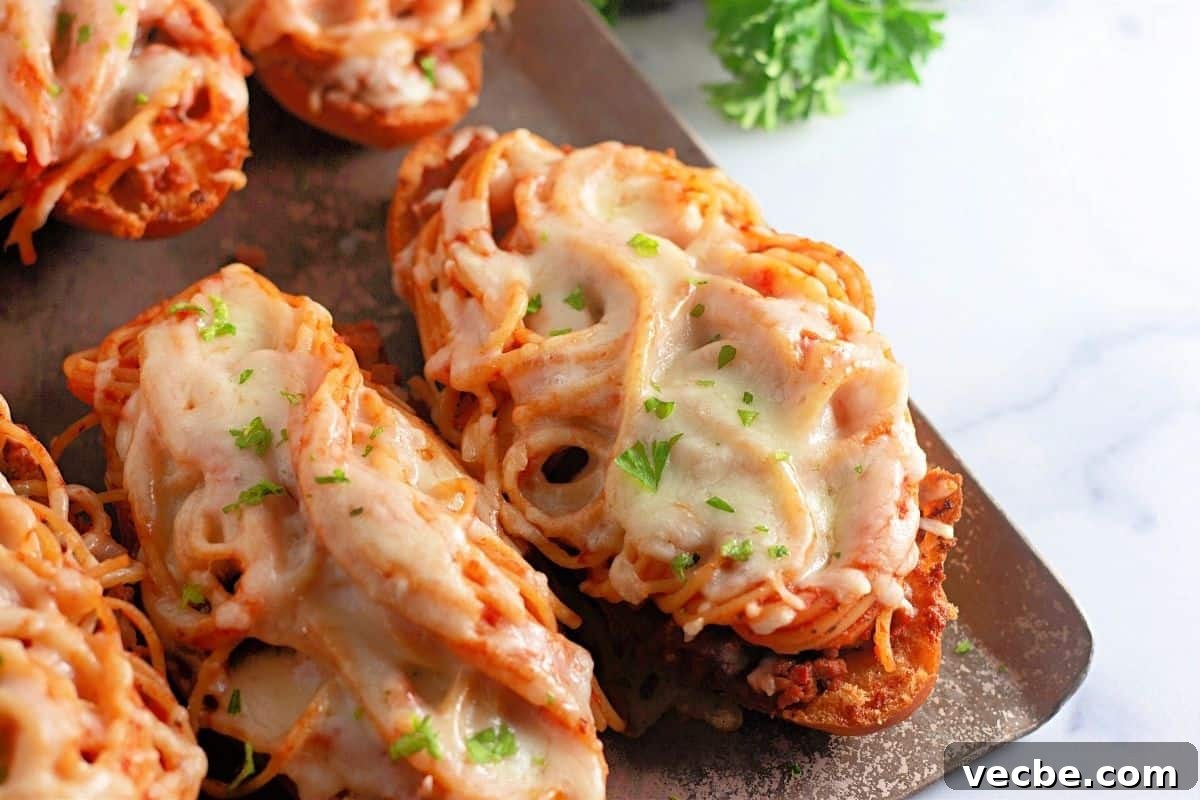25 Ground Beef Recipes for Real Weeknight Dinners 12 Toasted bread slices topped with spaghetti, meat sauce, melted cheese, and garnished with chopped parsley on a metal baking sheet.
