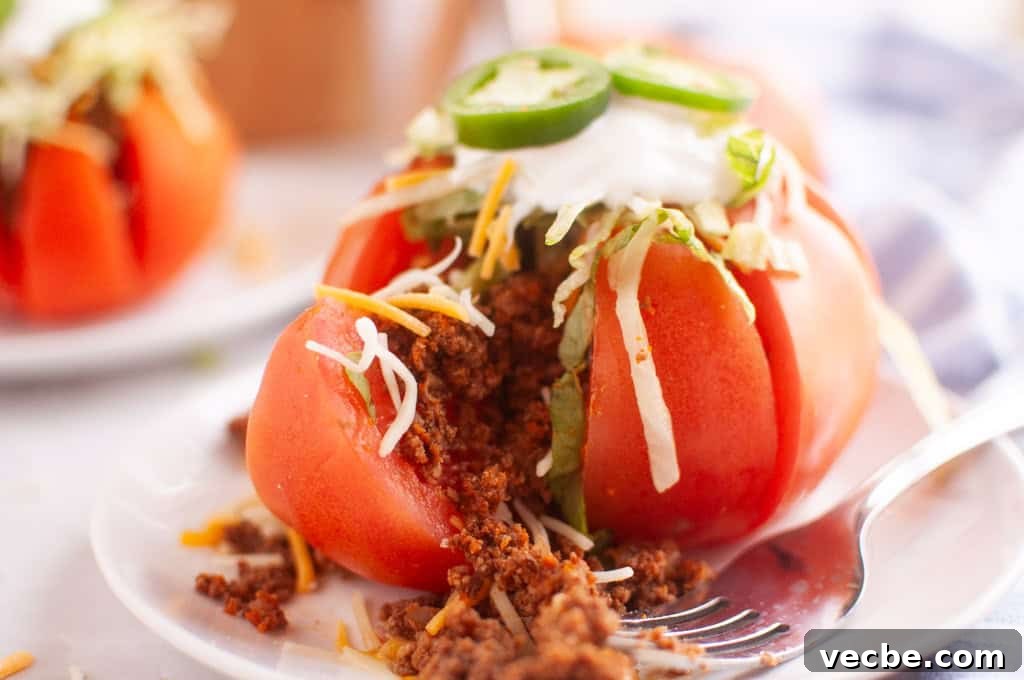 25 Ground Beef Recipes for Real Weeknight Dinners 13 A sliced tomato stuffed with seasoned ground meat, shredded cheese, lettuce, sour cream, and jalapeño slices is served on a white plate with a fork.