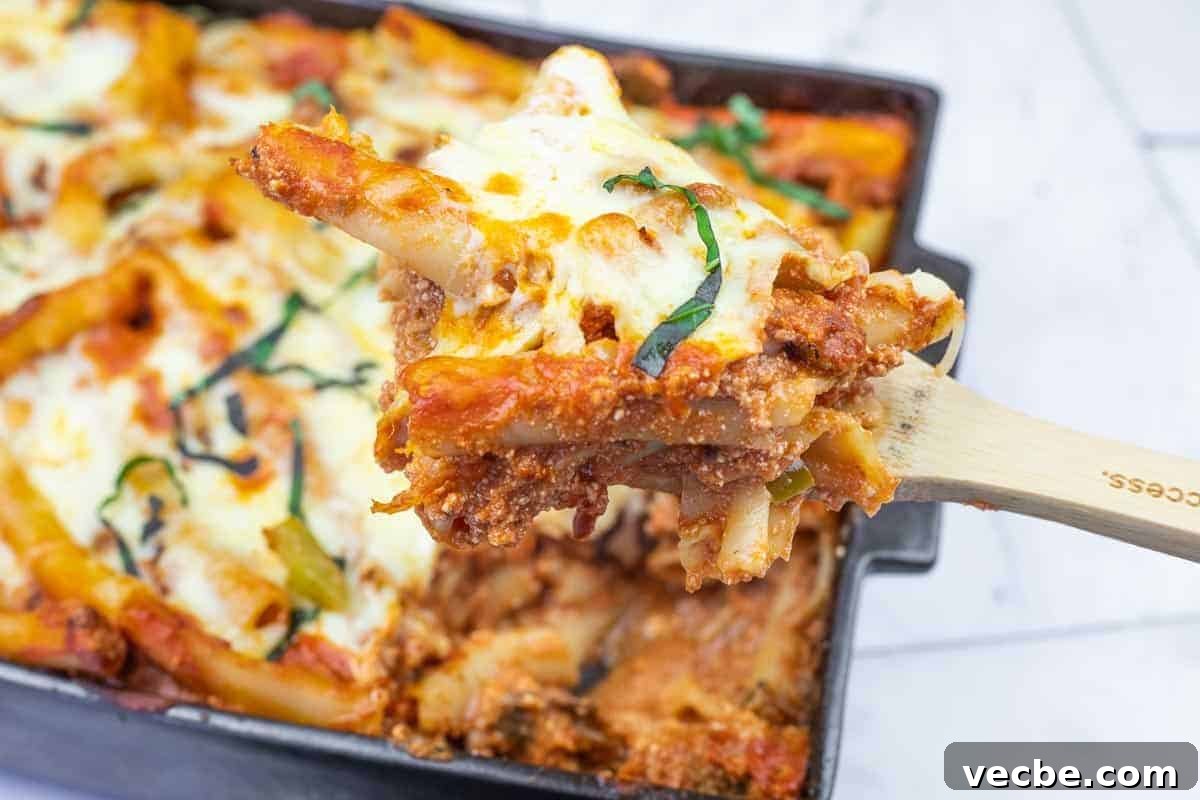 25 Ground Beef Recipes for Real Weeknight Dinners 20 A close-up of a wooden spoon lifting a serving of baked ziti with melted cheese and tomato sauce from a casserole dish.
