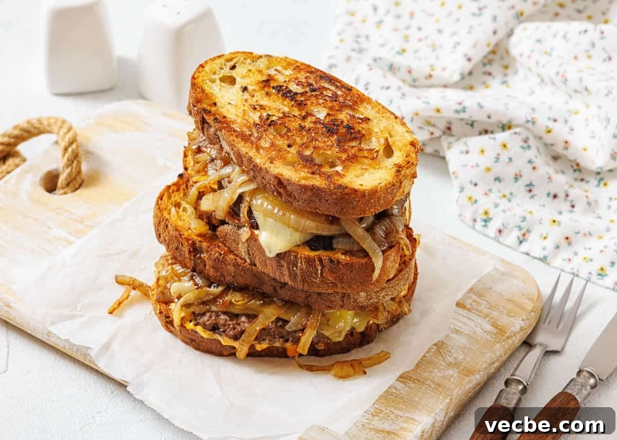25 Ground Beef Recipes for Real Weeknight Dinners 4 A stack of two patty melt sandwiches with caramelized onions and melted cheese on toasted bread, placed on parchment paper atop a wooden board.