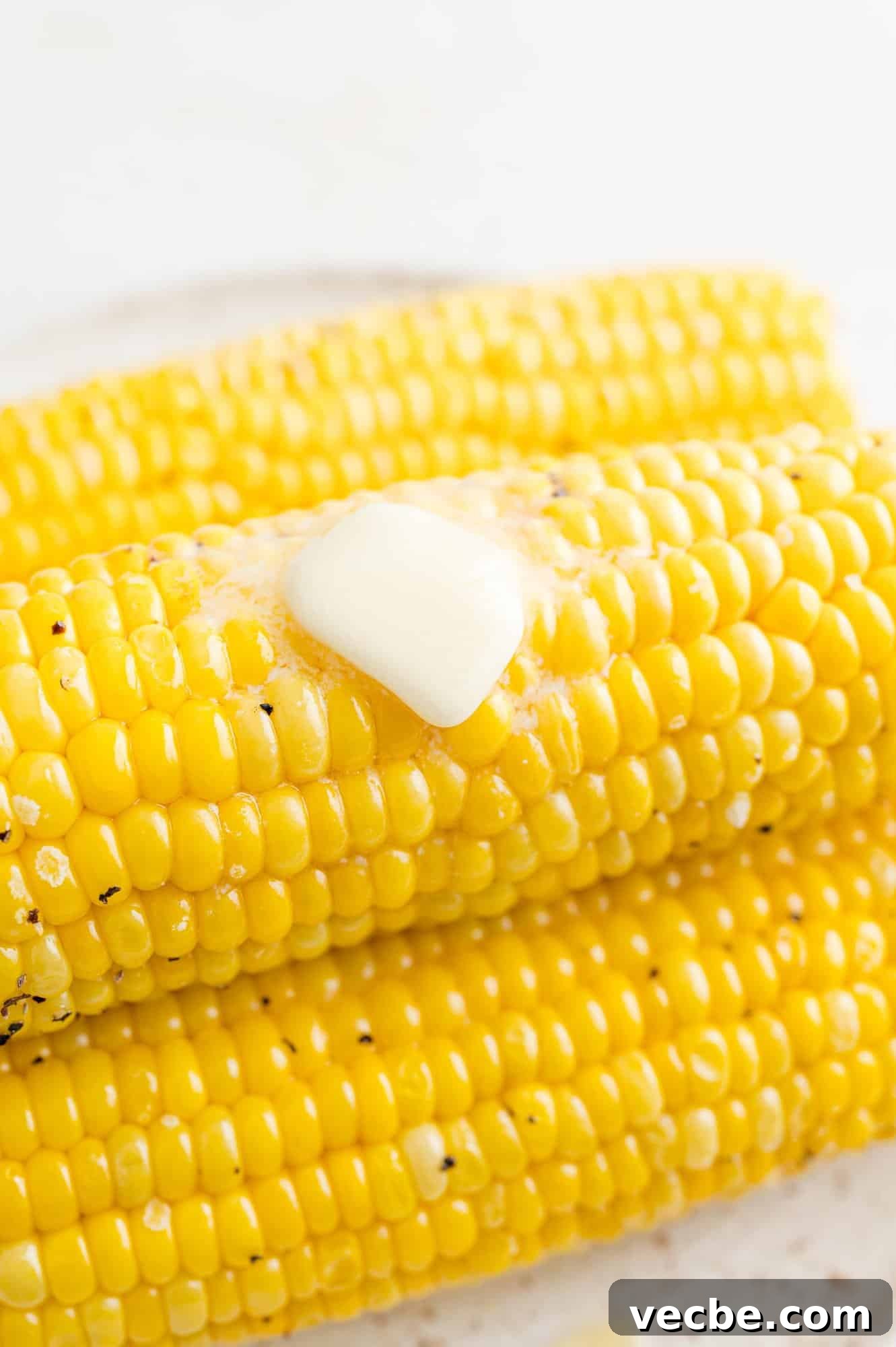 Air fryer corn on the cob is a quick and easy method for perfectly roasted corn! It's the perfect side for your favorite summer meals. Close up of a pat of butter melting over a stack of air fryer corn on the cob.