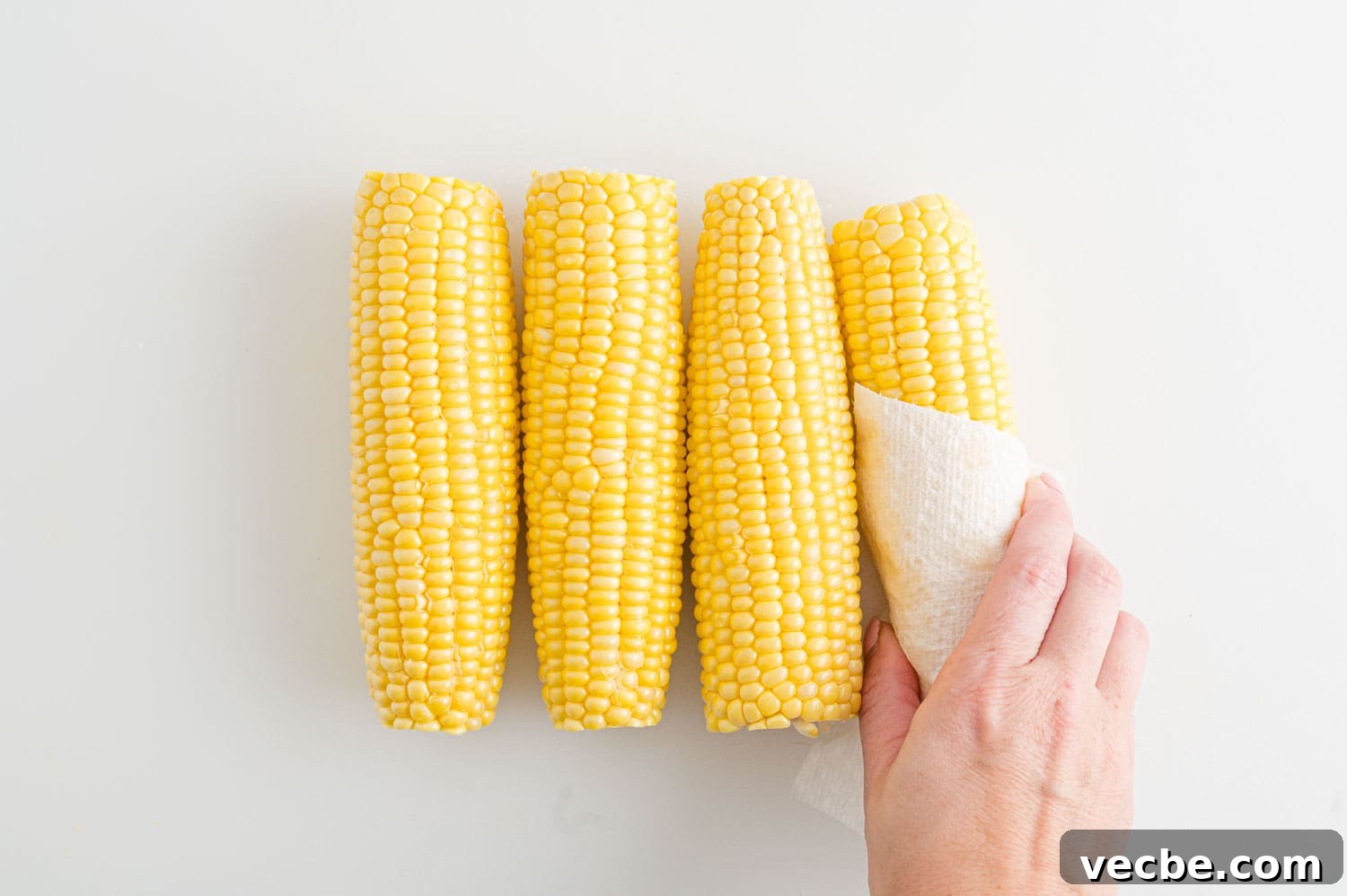 Crispy Buttered Air Fryer Corn on the Cob 4 A hand uses a paper towel to pat corn on the cob dry after rinsing.
