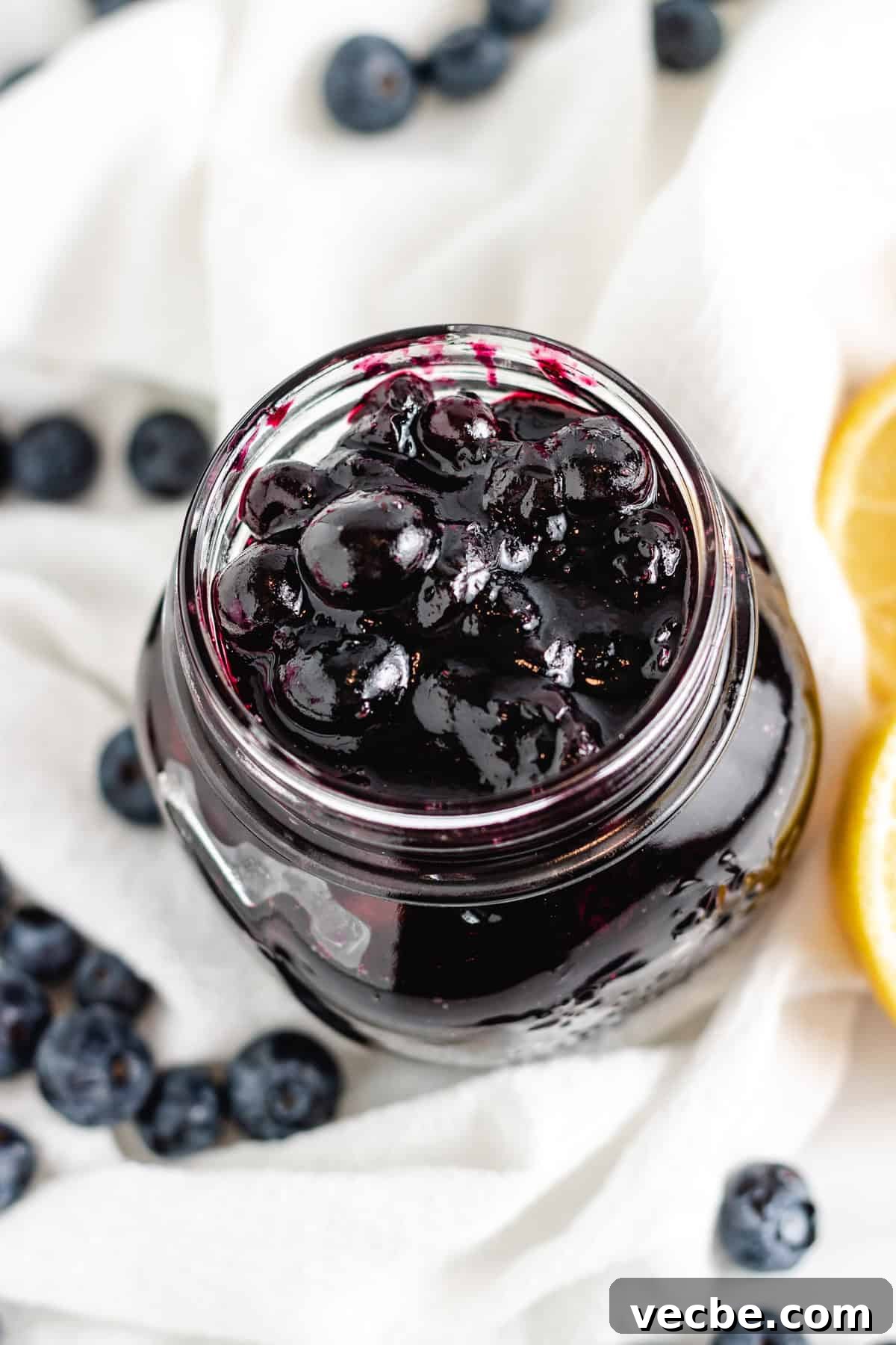 Blueberry Compote: Fresh Sauce for Yogurt and Pancakes 2 A top-down view of a jar filled with rich blueberry compote, with fresh blueberries scattered around and lemon slices on the side.