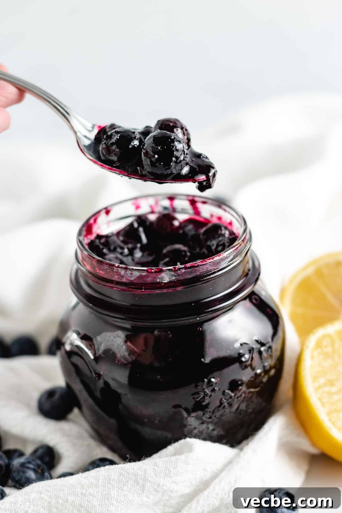 Blueberry Compote: Fresh Sauce for Yogurt and Pancakes 3 A spoonful of thick blueberry compote being lifted from a jar, surrounded by fresh blueberries and lemon slices.