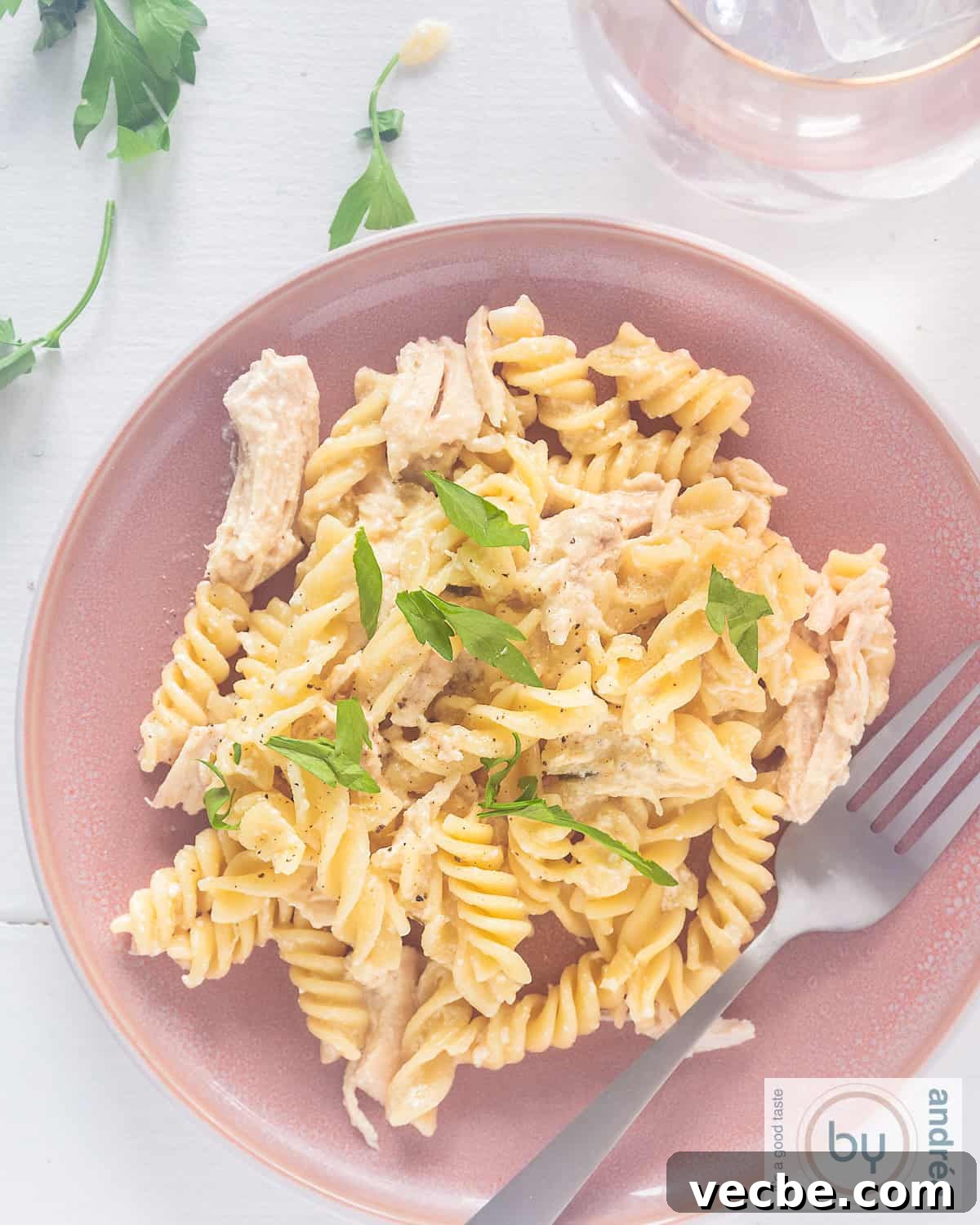 Slow Cooker Garlic Parmesan Chicken with Fusilli 2 A top-down photo of a pink plate with pasta, chicken and parmesan garlic sauce.