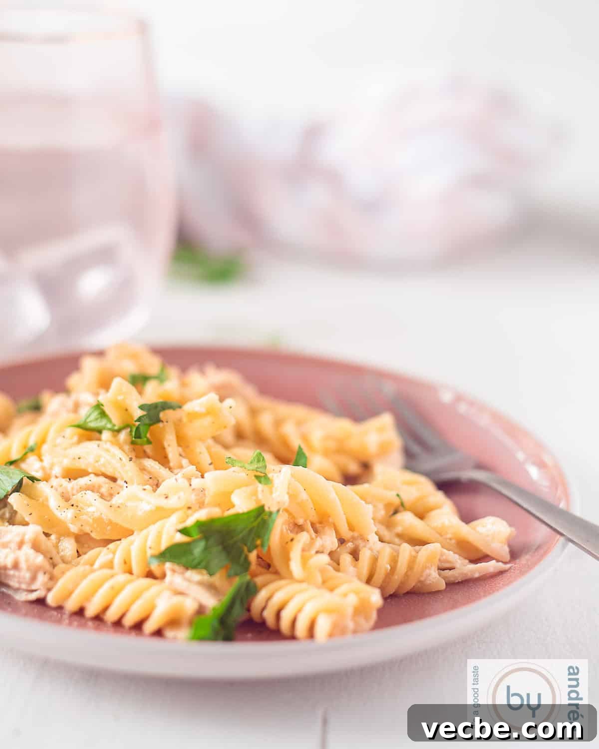 Slow Cooker Garlic Parmesan Chicken with Fusilli 5 An aerial photo with a pink plate of fusilli with chicken, garlic parmesan sauce, parsley. In the background pink glasses with water