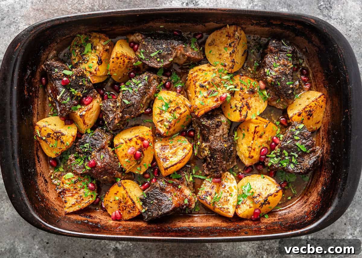 Greek Lemon Pot Roast with Crispy Potatoes 5 overhead: pot roast with potato wedges and pomegranate arils in a baking dish