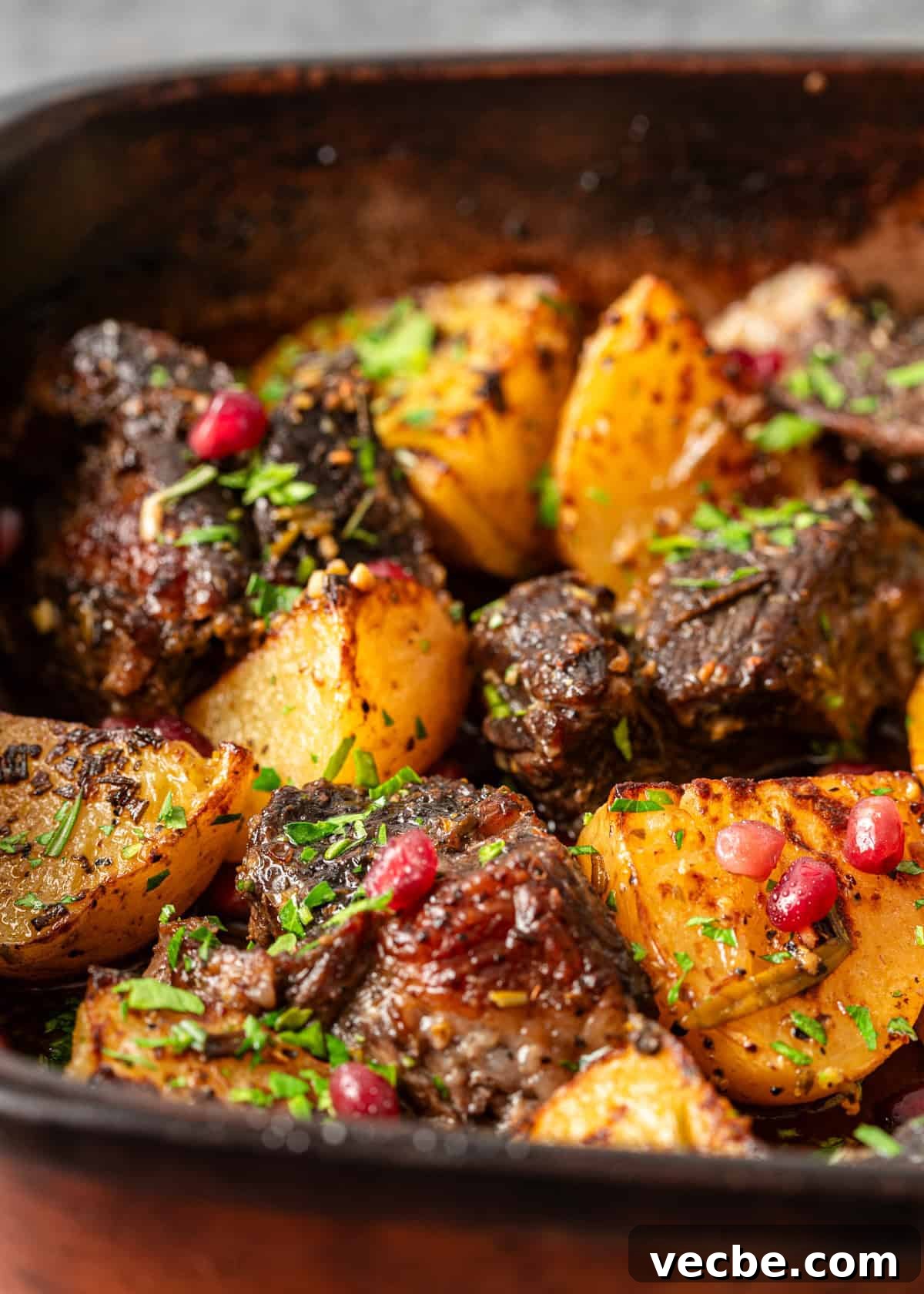 Greek Lemon Pot Roast with Crispy Potatoes 6 closeup: pot roast in oven with potatoes, herbs, and pomegranate arils