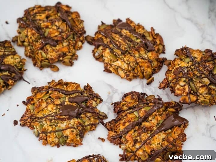 Homemade granola cookies with seeds and nuts, drizzled with dark chocolate, on a marble surface.