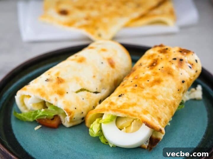 Two breakfast wraps containing boiled eggs, lettuce, and other ingredients are served on a teal plate with more wraps in the background.