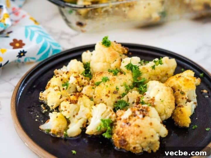 Keto roasted cauliflower on a black plate, garnished with parsley, with a glass baking dish in the background.