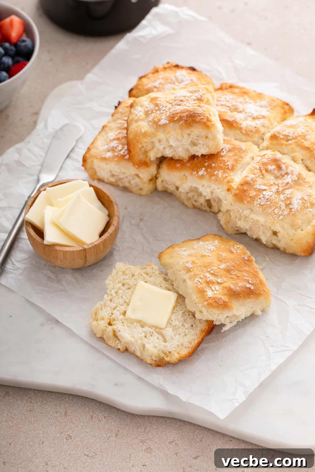 Fluffy 7-Up Biscuits Recipe 2 Buttered 7up biscuit next to butter and more biscuits on parchment paper.