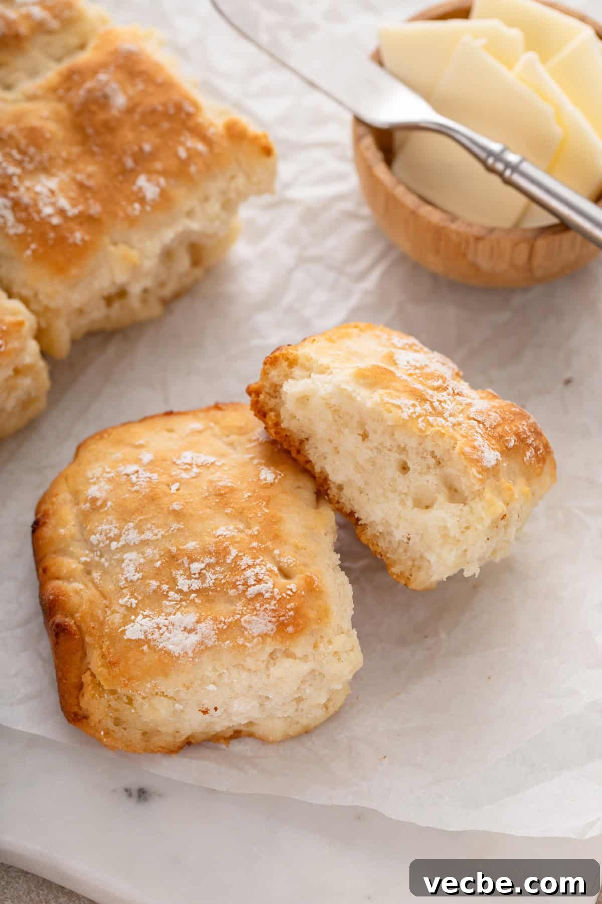 Fluffy 7-Up Biscuits Recipe 3 7up biscuits next to a bowl of butter on a piece of parchment paper.