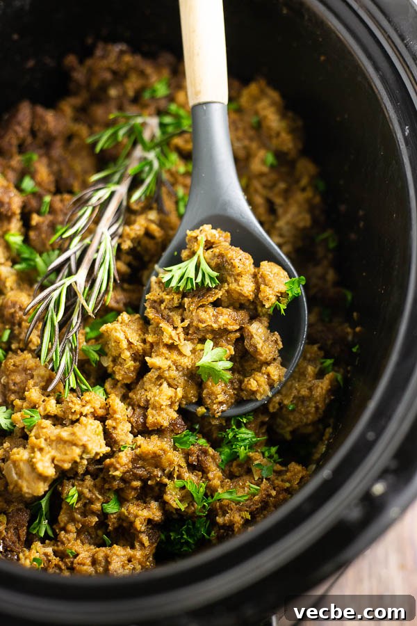 Herbed Slow Cooker Stuffing for Holiday Dinners 2 Wooden spoon in a black crock filled with stuffing and a rosemary sprig.