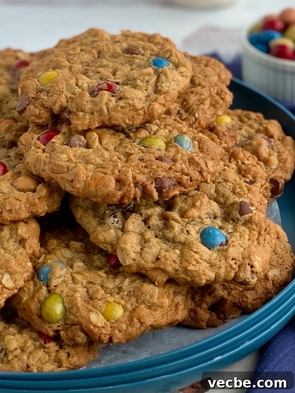 A blue plate with cookies stacked on it next to bowl of chocolate candies and a glass of milk.